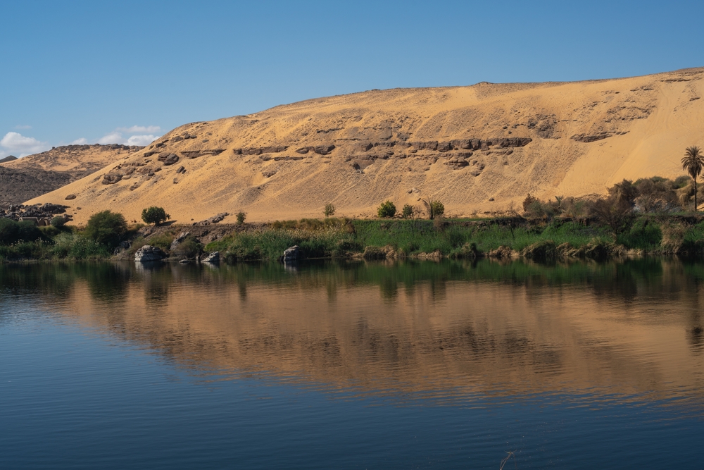 Sunrise over the Nile River near Luxor with temple silhouettes and a traditional felucca on calm water.”